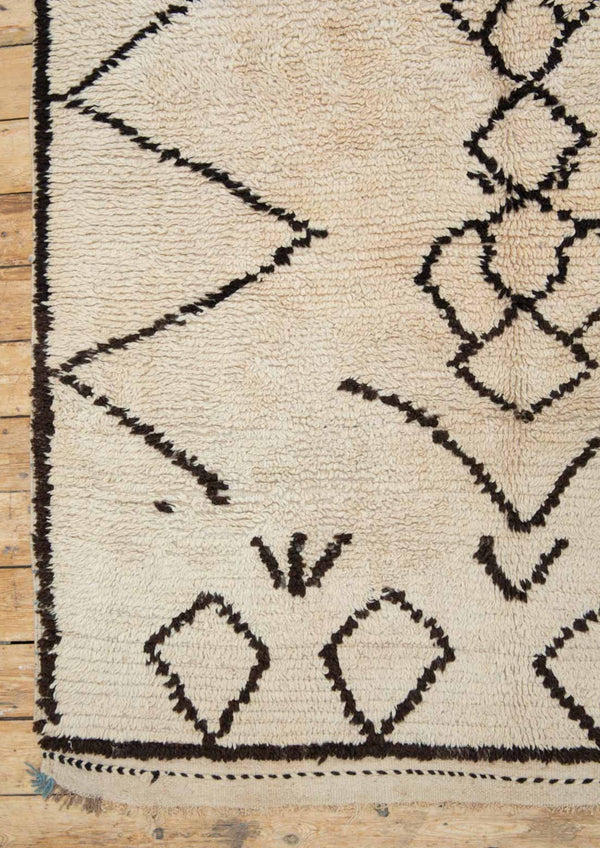 A traditional Azilal Moroccan rug featuring geometric patterns with black and beige colors on a beige background.