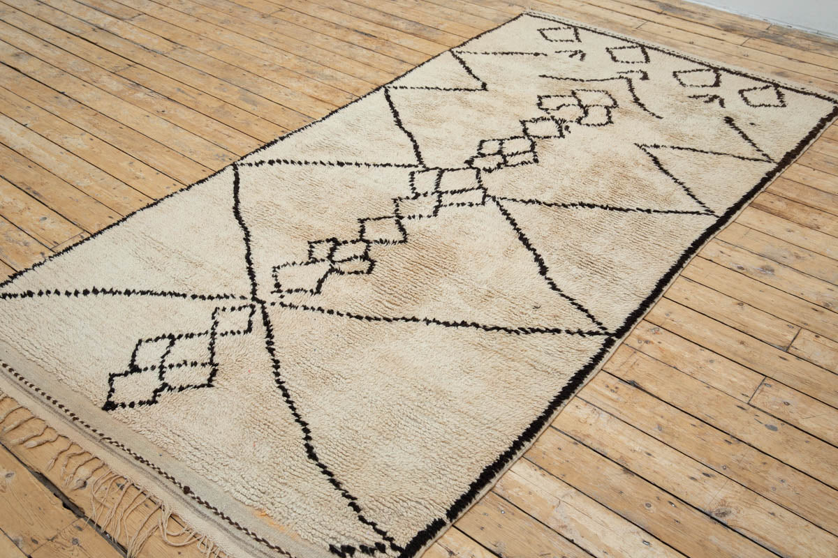 A traditional Azilal Moroccan rug featuring geometric patterns with black and beige colors on a beige background.