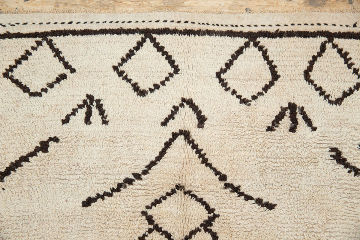 A traditional Azilal Moroccan rug featuring geometric patterns with black and beige colors on a beige background.
