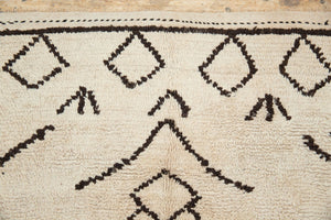 A traditional Azilal Moroccan rug featuring geometric patterns with black and beige colors on a beige background.