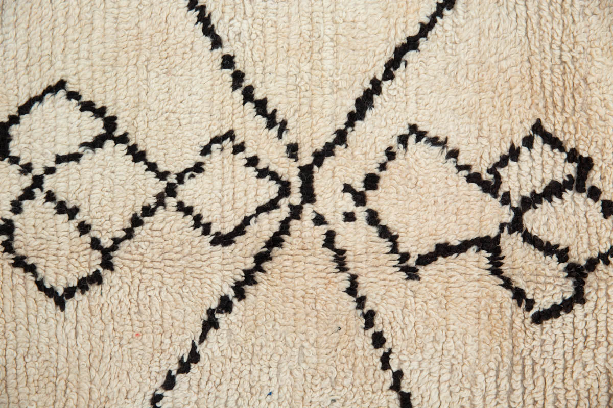 A traditional Azilal Moroccan rug featuring geometric patterns with black and beige colors on a beige background.