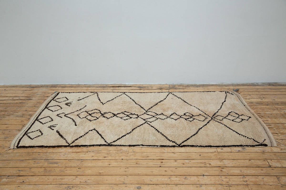 A traditional Azilal Moroccan rug featuring geometric patterns with black and beige colors on a beige background.