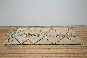 A traditional Azilal Moroccan rug featuring geometric patterns with black and beige colors on a beige background.