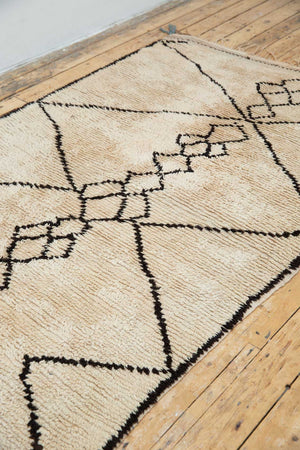 A traditional Azilal Moroccan rug featuring geometric patterns with black and beige colors on a beige background.