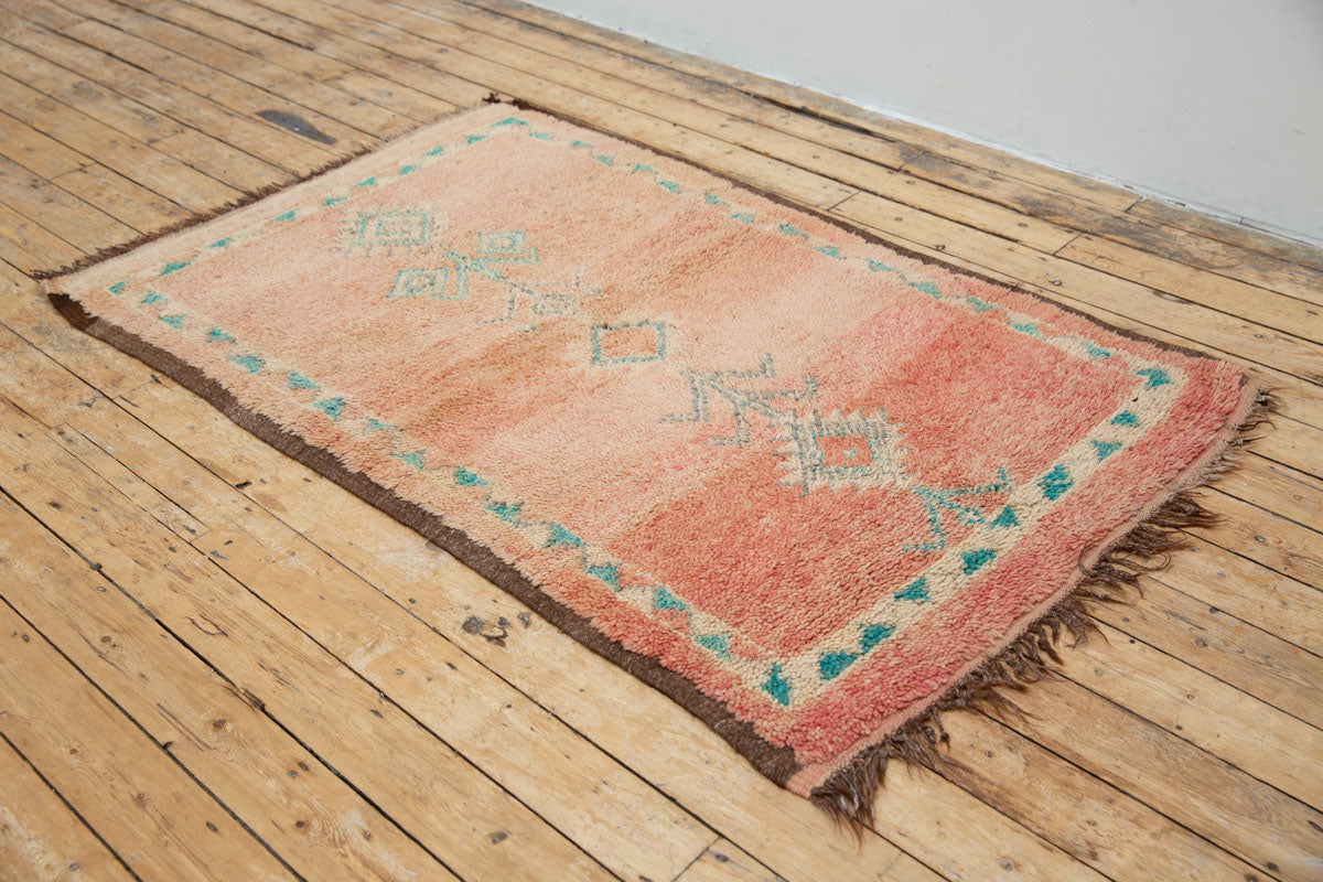 A vintage Boujad rug with a peach and sage green color palette, featuring geometric patterns and berber symbology, approximately 40 years old