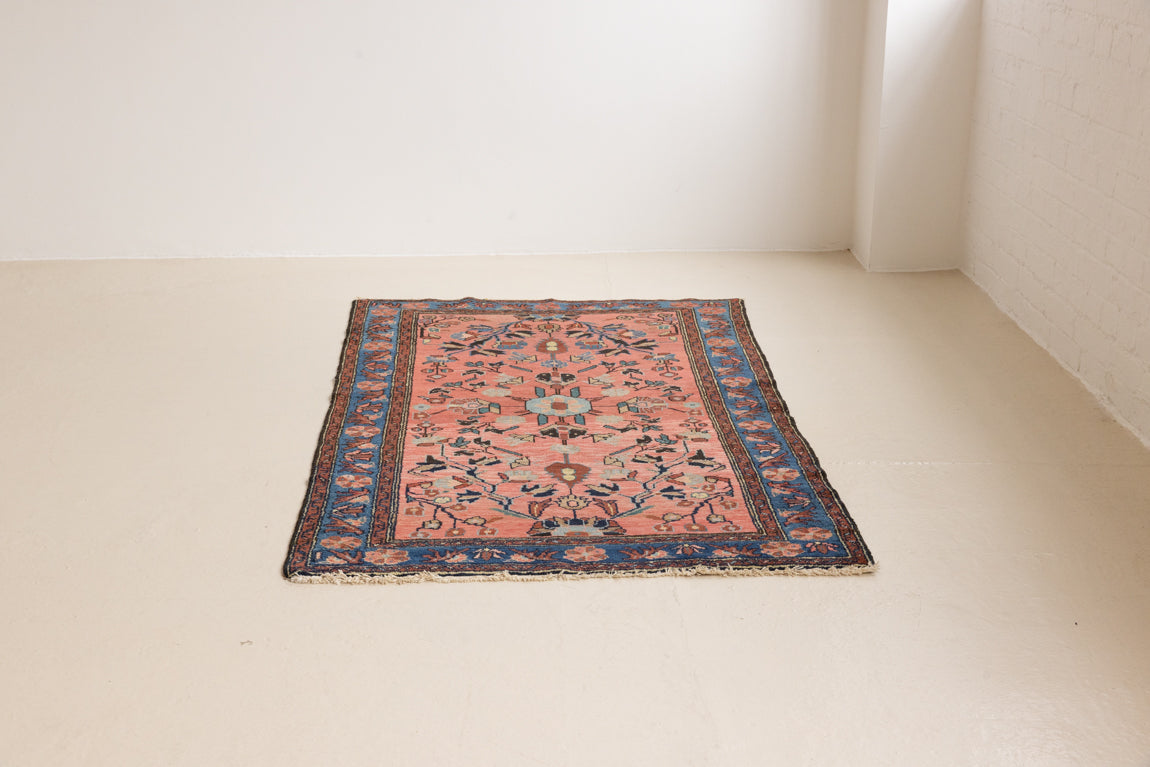 Lilian rugs were handwoven in a small village in Western Iran and often feature floral and geometric patterns as seen here. This small vintage carpet features a soft pink and blue colour palette and an intricate design inspired by nature.