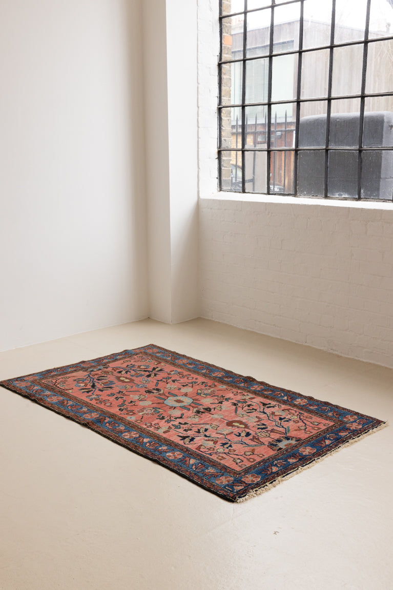 Lilian rugs were handwoven in a small village in Western Iran and often feature floral and geometric patterns as seen here. This small vintage carpet features a soft pink and blue colour palette and an intricate design inspired by nature.