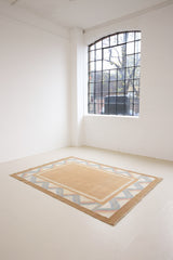 A Swedish geometric-patterned rug with multicolor border on a beige background. This röllakan rug was handwoven by the mid-century textile designer Anna Johanna Angström.