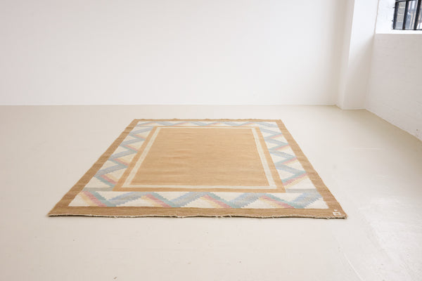 A Swedish geometric-patterned rug with multicolor border on a beige background. This röllakan rug was handwoven by the mid-century textile designer Anna Johanna Angström.