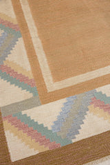 A Swedish geometric-patterned rug with multicolor border on a beige background. This röllakan rug was handwoven by the mid-century textile designer Anna Johanna Angström.