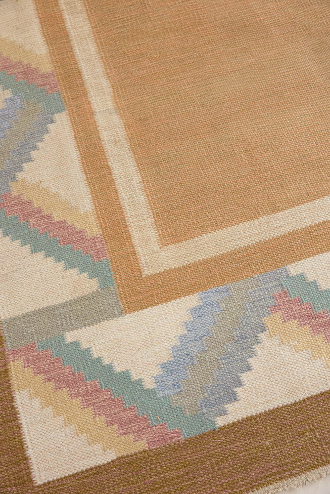 A Swedish geometric-patterned rug with multicolor border on a beige background. This röllakan rug was handwoven by the mid-century textile designer Anna Johanna Angström.