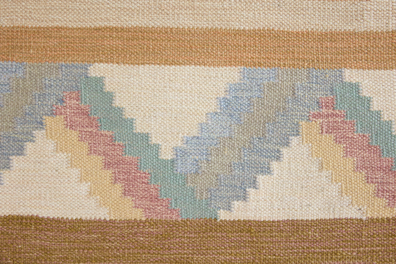A Swedish geometric-patterned rug with multicolor border on a beige background. This röllakan rug was handwoven by the mid-century textile designer Anna Johanna Angström.
