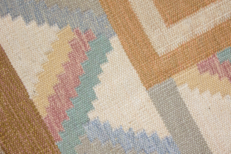 A Swedish geometric-patterned rug with multicolor border on a beige background. This röllakan rug was handwoven by the mid-century textile designer Anna Johanna Angström.