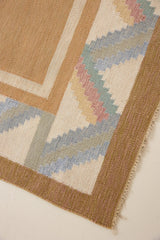 A Swedish geometric-patterned rug with multicolor border on a beige background. This röllakan rug was handwoven by the mid-century textile designer Anna Johanna Angström.
