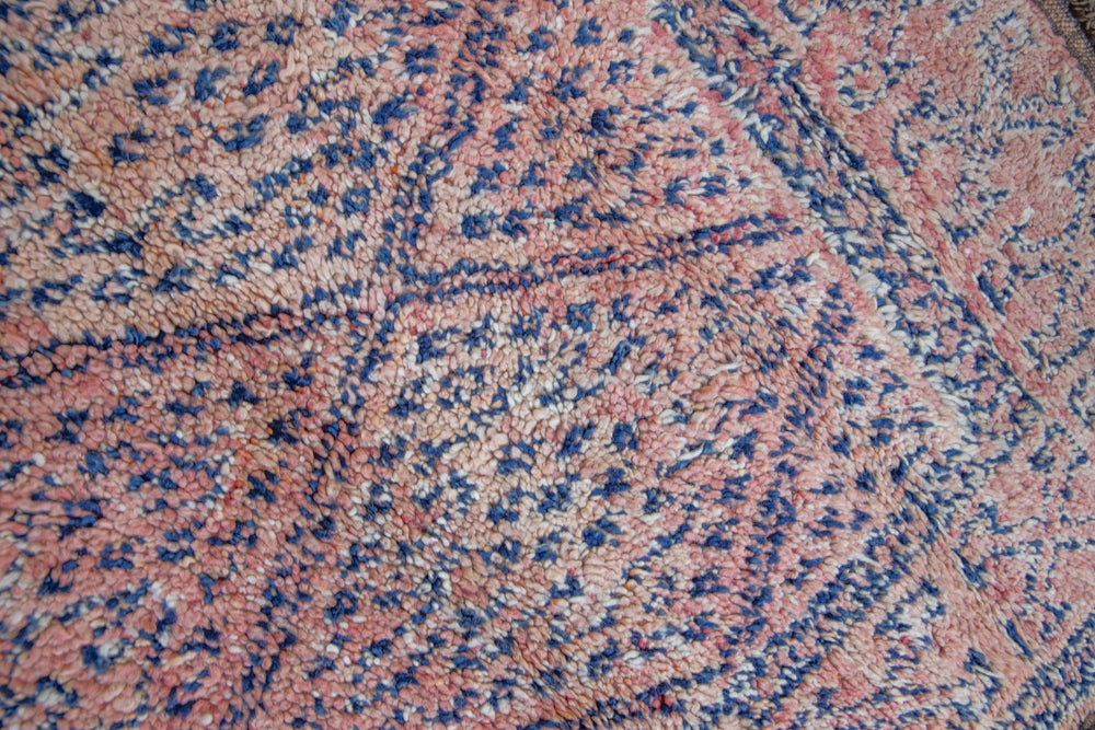 Beni M’guild thick piled carpet. Rug features a dark blue geometric pattern on a peachy pink background.