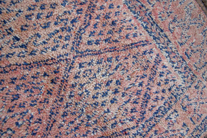 Beni M’guild thick piled carpet. Rug features a dark blue geometric pattern on a peachy pink background.