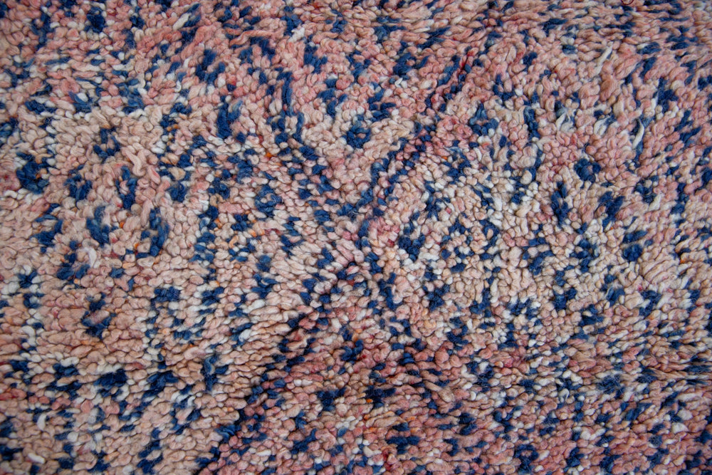 Beni M’guild thick piled carpet. Rug features a dark blue geometric pattern on a peachy pink background.