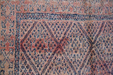 Beni M’guild thick piled carpet. Rug features a dark blue geometric pattern on a peachy pink background.