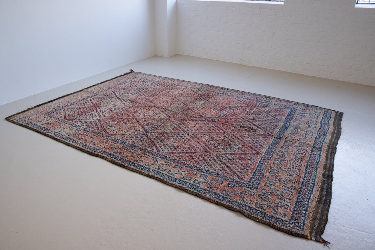 Beni M’guild thick piled carpet. Rug features a dark blue geometric pattern on a peachy pink background.