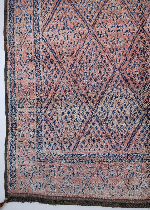 Beni M’guild thick piled carpet. Rug features a dark blue geometric pattern on a peachy pink background.