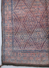 Beni M’guild thick piled carpet. Rug features a dark blue geometric pattern on a peachy pink background.