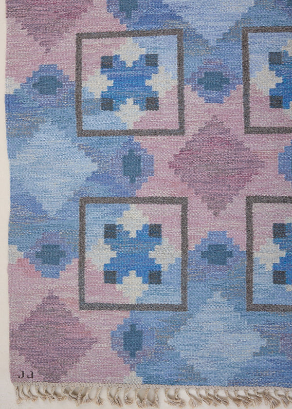 A striking flatweave Swedish rug with geometric pattern featuring blue, purple, and white colours. handwoven in Sweden by textile designer Judith Johanasson.