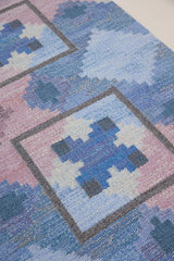 A striking flatweave Swedish rug with geometric pattern featuring blue, purple, and white colours. handwoven in Sweden by textile designer Judith Johanasson.