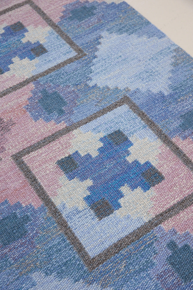 A striking flatweave Swedish rug with geometric pattern featuring blue, purple, and white colours. handwoven in Sweden by textile designer Judith Johanasson.