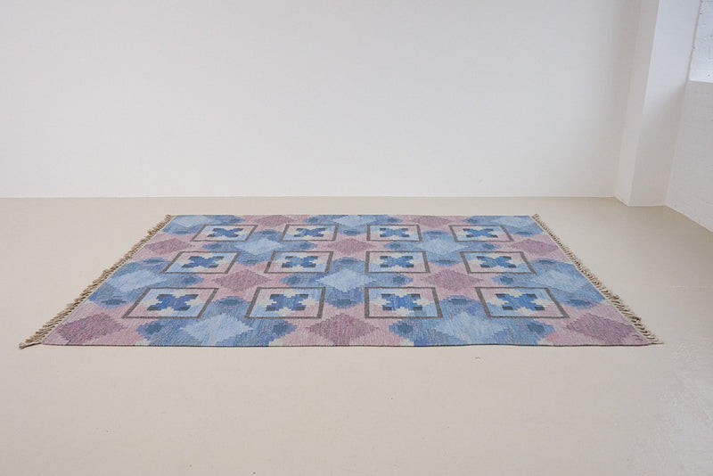 A striking flatweave Swedish rug with geometric pattern featuring blue, purple, and white colours. handwoven in Sweden by textile designer Judith Johanasson.