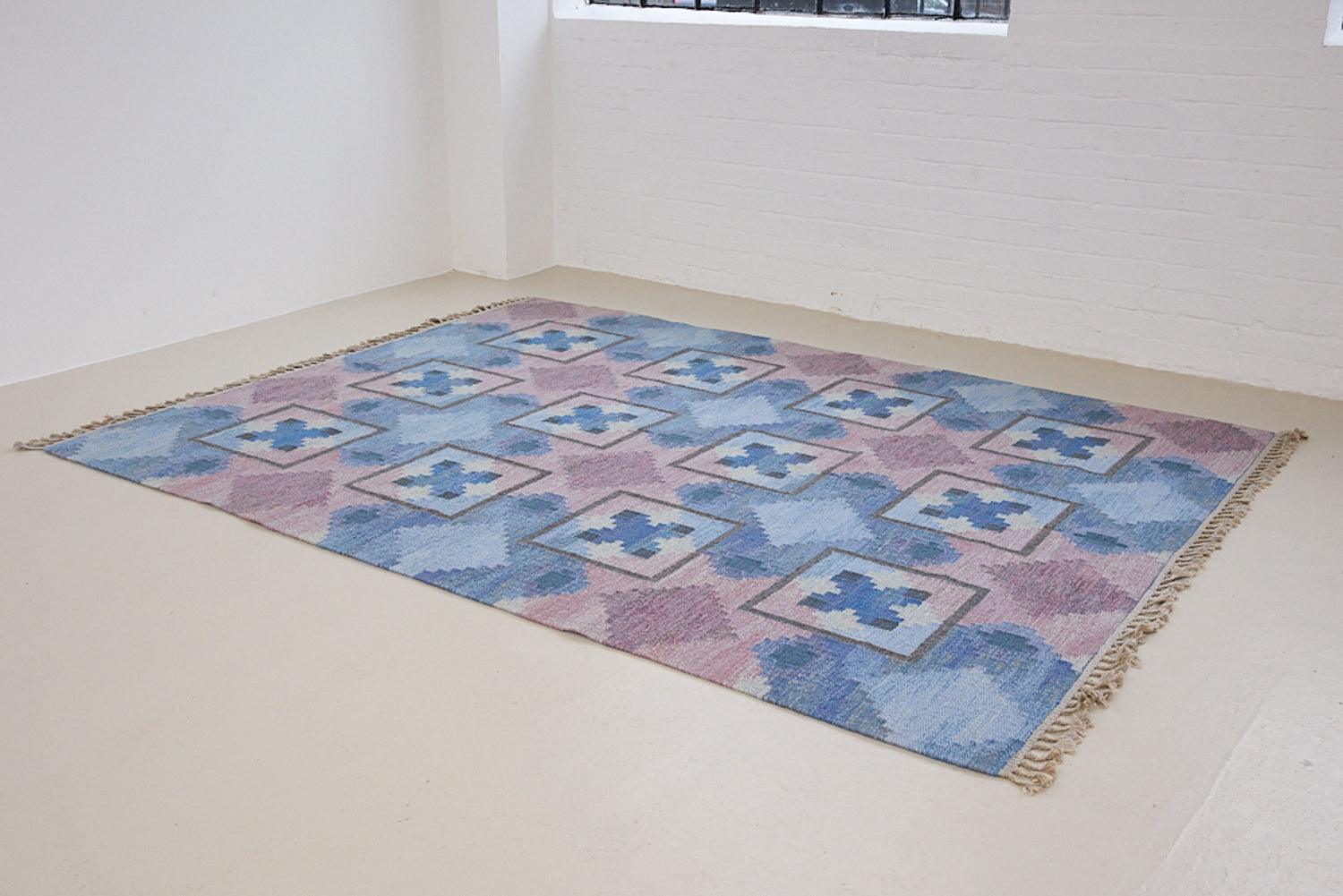 A striking flatweave Swedish rug with geometric pattern featuring blue, purple, and white colours. handwoven in Sweden by textile designer Judith Johanasson.