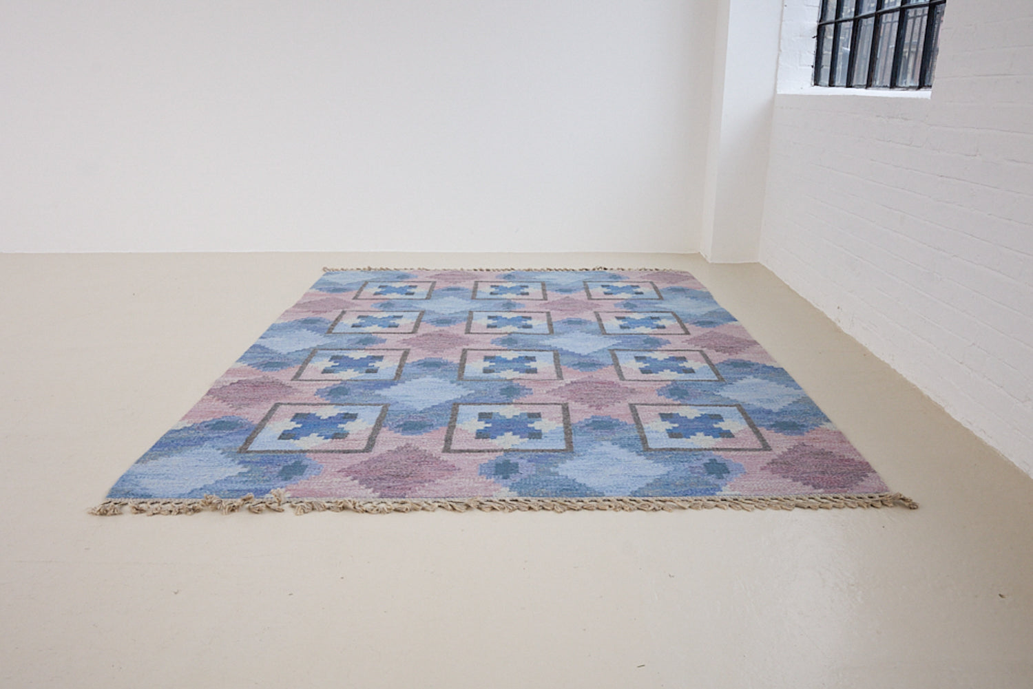 A striking flatweave Swedish rug with geometric pattern featuring blue, purple, and white colours. handwoven in Sweden by textile designer Judith Johanasson.