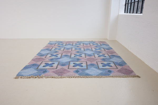 A striking flatweave Swedish rug with geometric pattern featuring blue, purple, and white colours. handwoven in Sweden by textile designer Judith Johanasson.