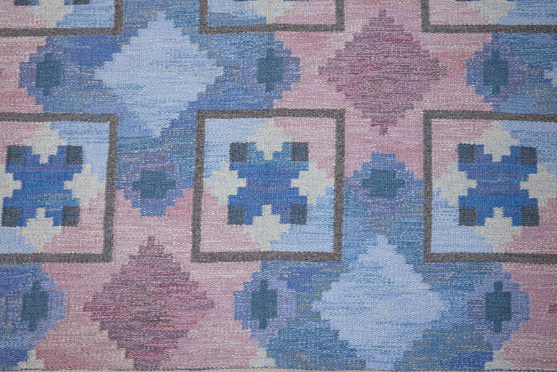 A striking flatweave Swedish rug with geometric pattern featuring blue, purple, and white colours. handwoven in Sweden by textile designer Judith Johanasson.