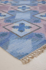 A striking flatweave Swedish rug with geometric pattern featuring blue, purple, and white colours. handwoven in Sweden by textile designer Judith Johanasson.
