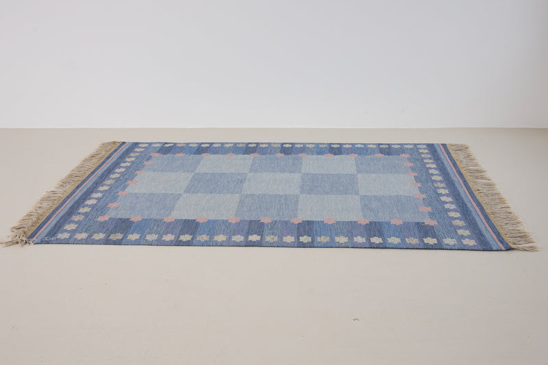 an original Swedish röllakan rug handwoven by mid-century textile designer Anna Johanna Angström. Her colourful kilim features strong lines in a blue and pale blue checkered pattern with accents of pink and cream