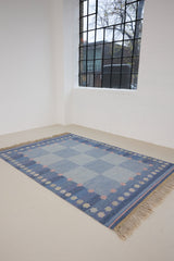 an original Swedish röllakan rug handwoven by mid-century textile designer Anna Johanna Angström. Her colourful kilim features strong lines in a blue and pale blue checkered pattern with accents of pink and cream