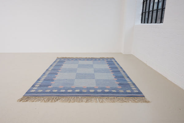 an original Swedish röllakan rug handwoven by mid-century textile designer Anna Johanna Angström. Her colourful kilim features strong lines in a blue and pale blue checkered pattern with accents of pink and cream
