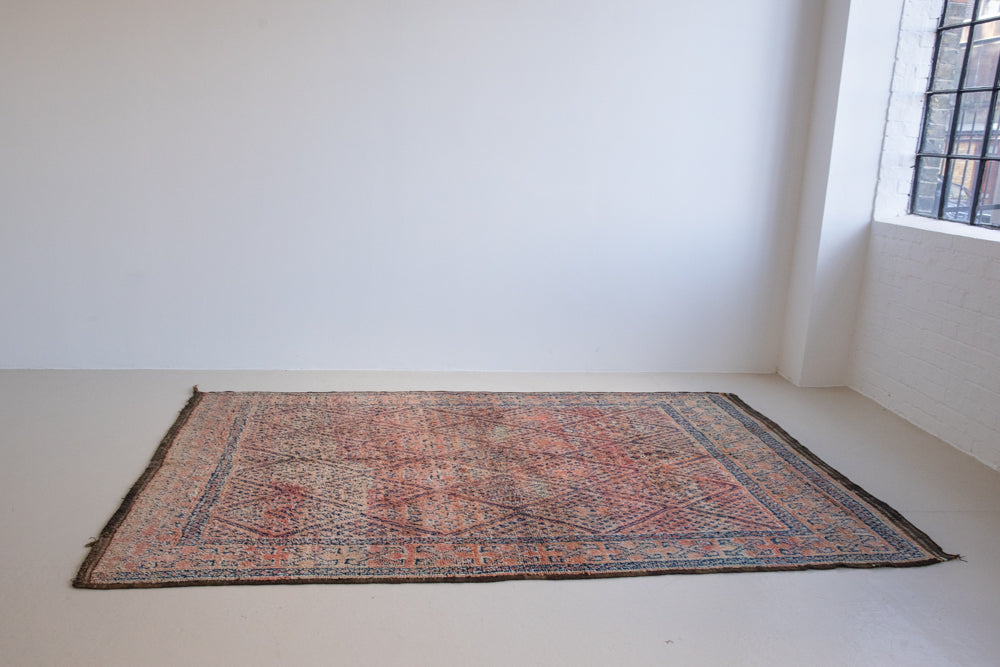 Beni M’guild thick piled carpet. Rug features a dark blue geometric pattern on a peachy pink background.