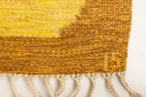 A vintage flatweave rug with geometric and floral patterns in yellow, beige, and other colors, with a brown border and white tassels. Barbara is a röllakan rug handwoven by designer Ingegerd Silow.