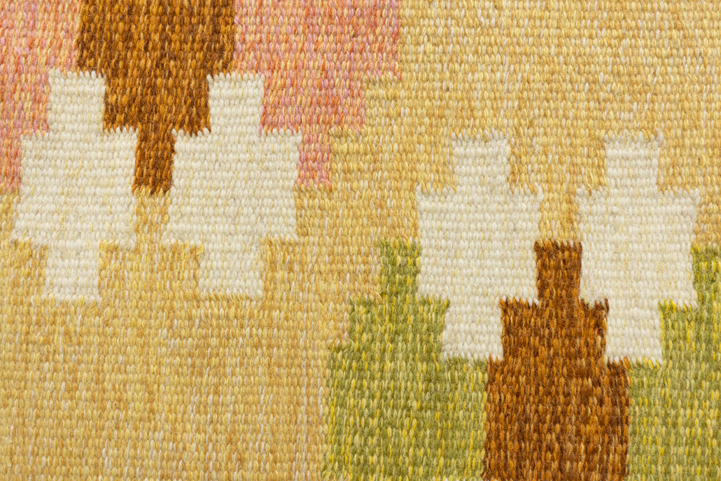 A vintage flatweave rug with geometric and floral patterns in yellow, beige, and other colors, with a brown border and white tassels. Barbara is a röllakan rug handwoven by designer Ingegerd Silow.